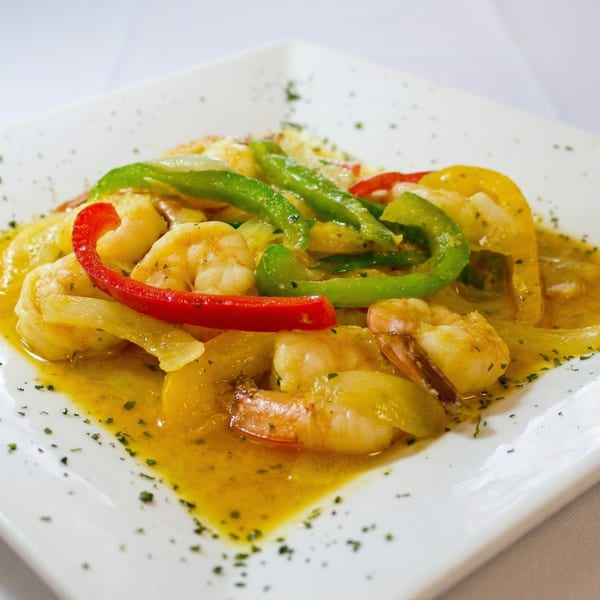 Shrimp and bell peppers in a yellow sauce, garnished with herbs on a white plate.