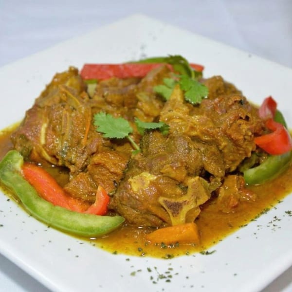 Curried goat with red and green bell peppers, carrots, and cilantro on a white plate.