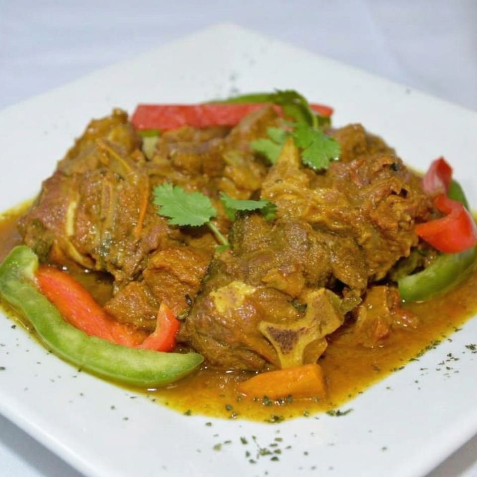 Curried goat with red and green bell peppers, carrots, and cilantro on a white plate.