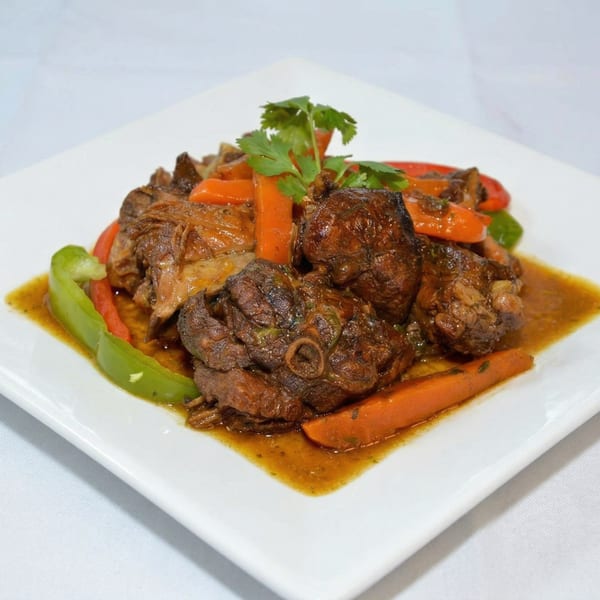 Braised oxtail stew with carrots, bell peppers, and cilantro on a white rectangular plate.
