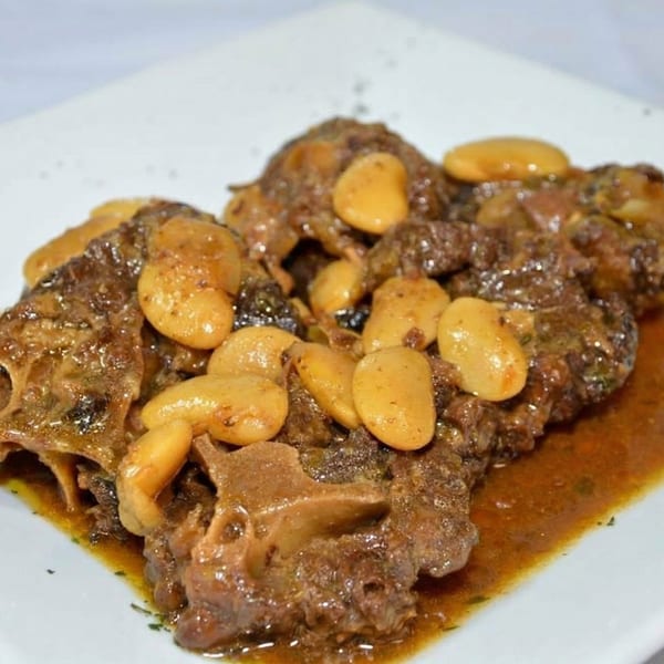 Close-up of oxtail stew with lima beans in a rich brown sauce on a white plate.