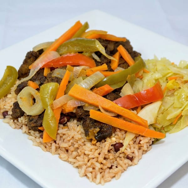 A plate of rice and peas topped with brown stew chicken, bell peppers, carrots, and cabbage.